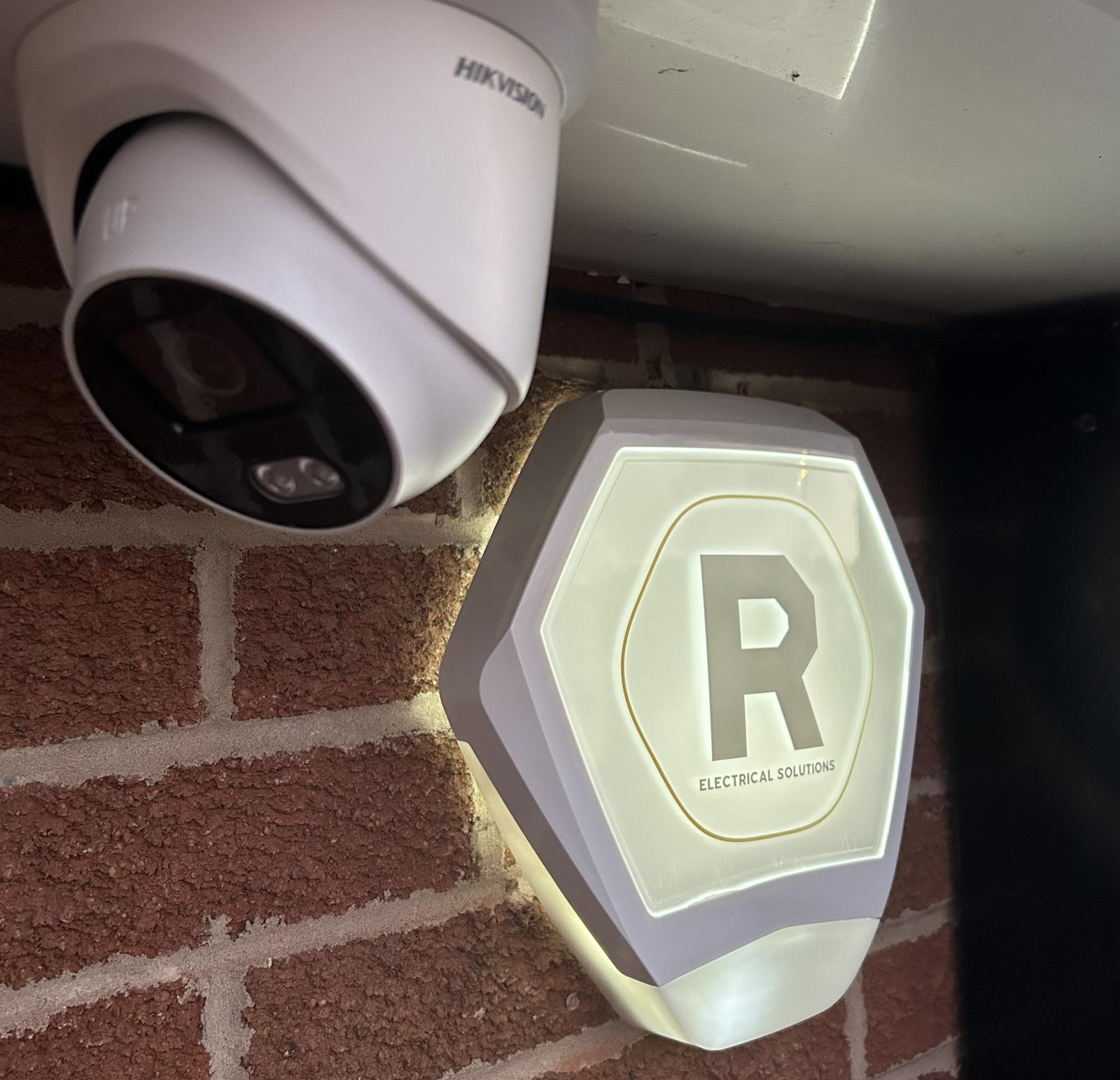 Hikvision dome CCTV camera and illuminated alarm sounder installed on a brick house wall