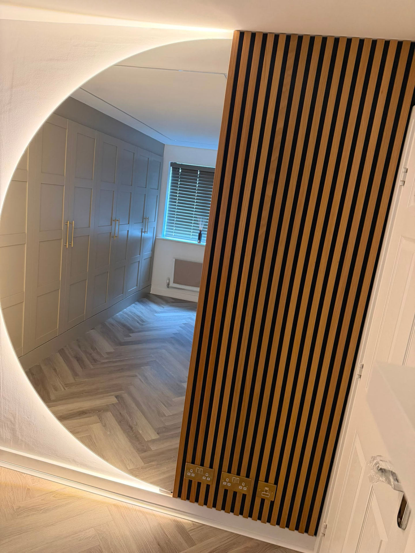 Circular backlit mirror lighting against a wooden slat wall panel